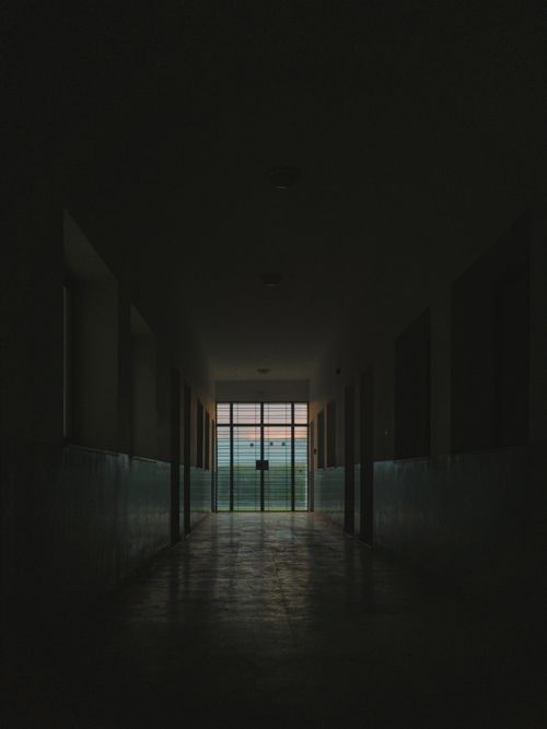 Free Explore the eerie ambiance of a dimly lit corridor leading to a glass door. Stock Photo