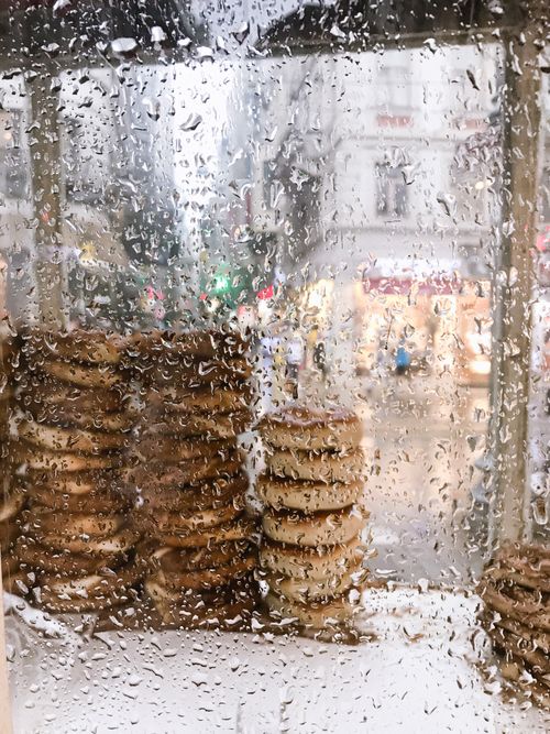 Free Wet window view showing stacked bagels and a busy street blurred in the background, captured on a rainy day. Stock Photo