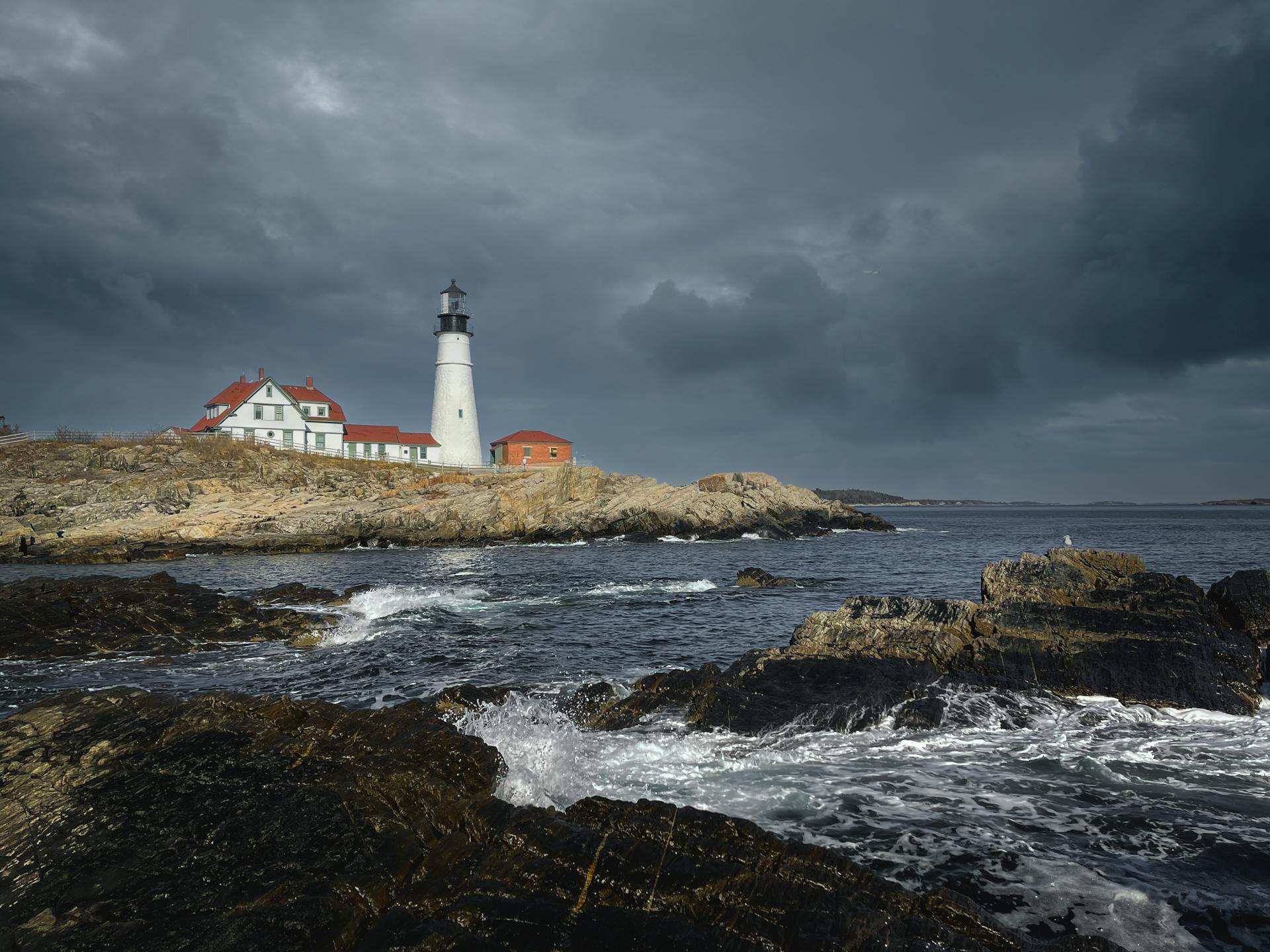 A striking lighthouse on a rocky coast under stormy skies, offering a dramatic marine view.