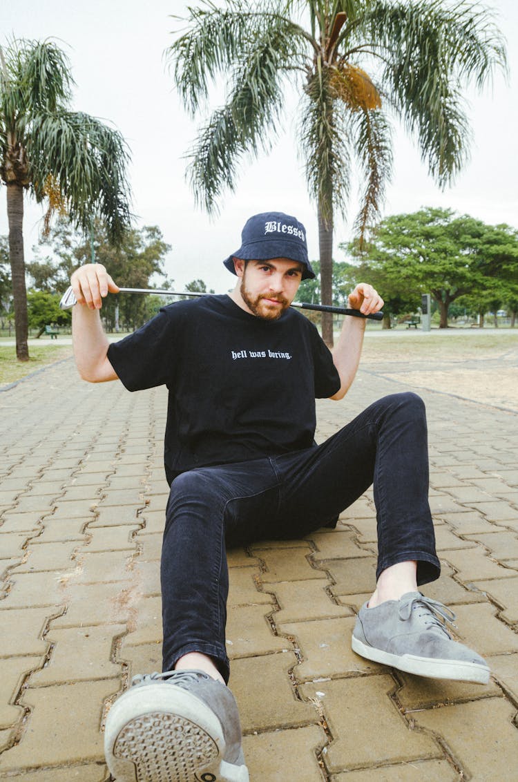 Man In Black T-shirt Sitting On Concrete Paving