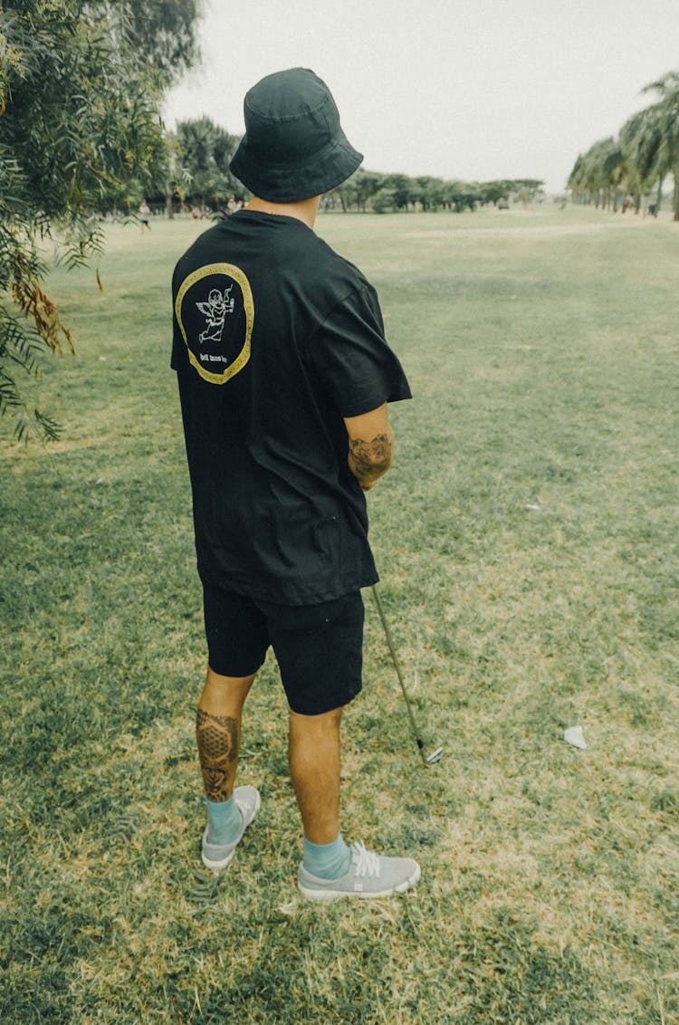 Man In Black Shirt Holding A Golf Club Standing On The Grass