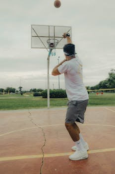 A man in a white t-shirt prepares to shoot a free throw on an outdoor basketball court.