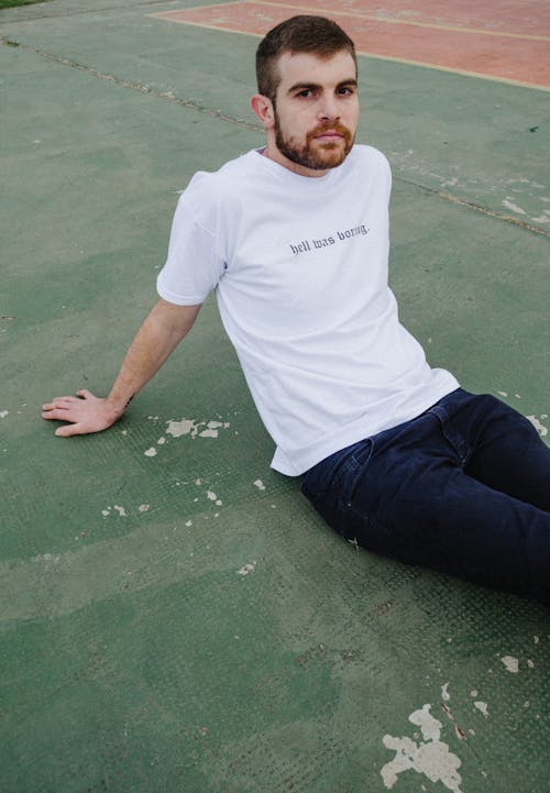 Man in Crew Neck T-shirt and Black Pants Sitting on Green Concrete Floor