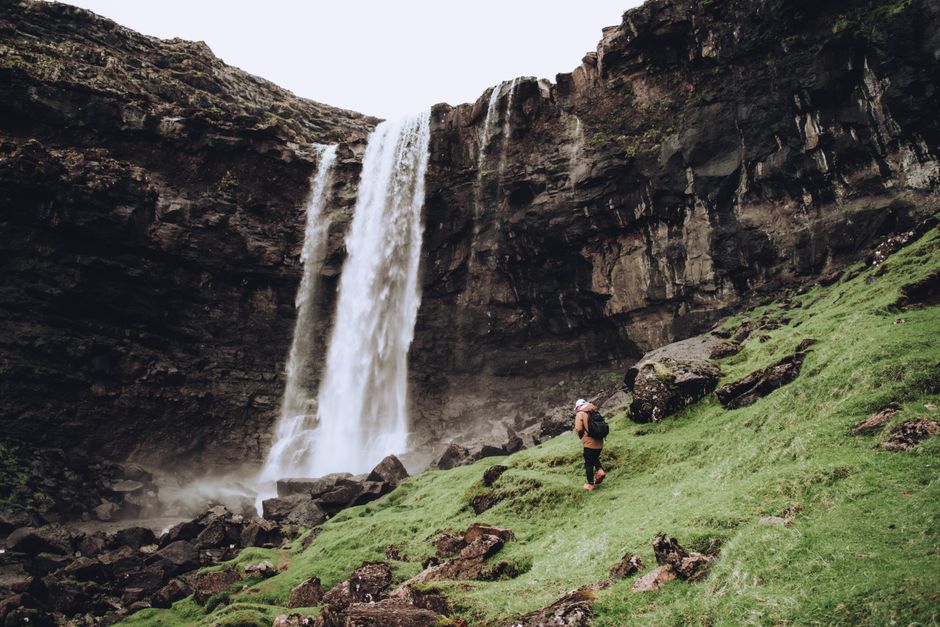 A lone backpacker explores the lush terrain near a breathtaking waterfall.