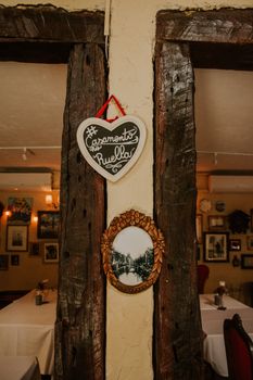 Decorative frames with inscription hanging on shabby wall between doorways of restaurant with tables with white cloth and paintings on wall
