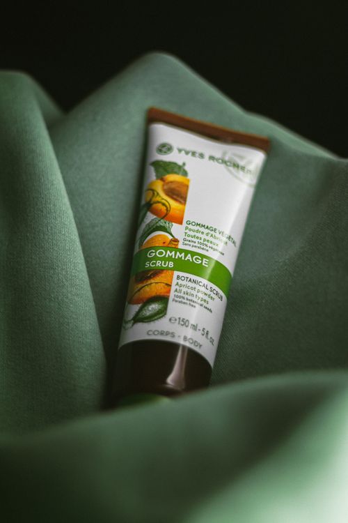 Free A botanical gommage scrub tube placed on a soft green fabric in a close-up shot. Stock Photo