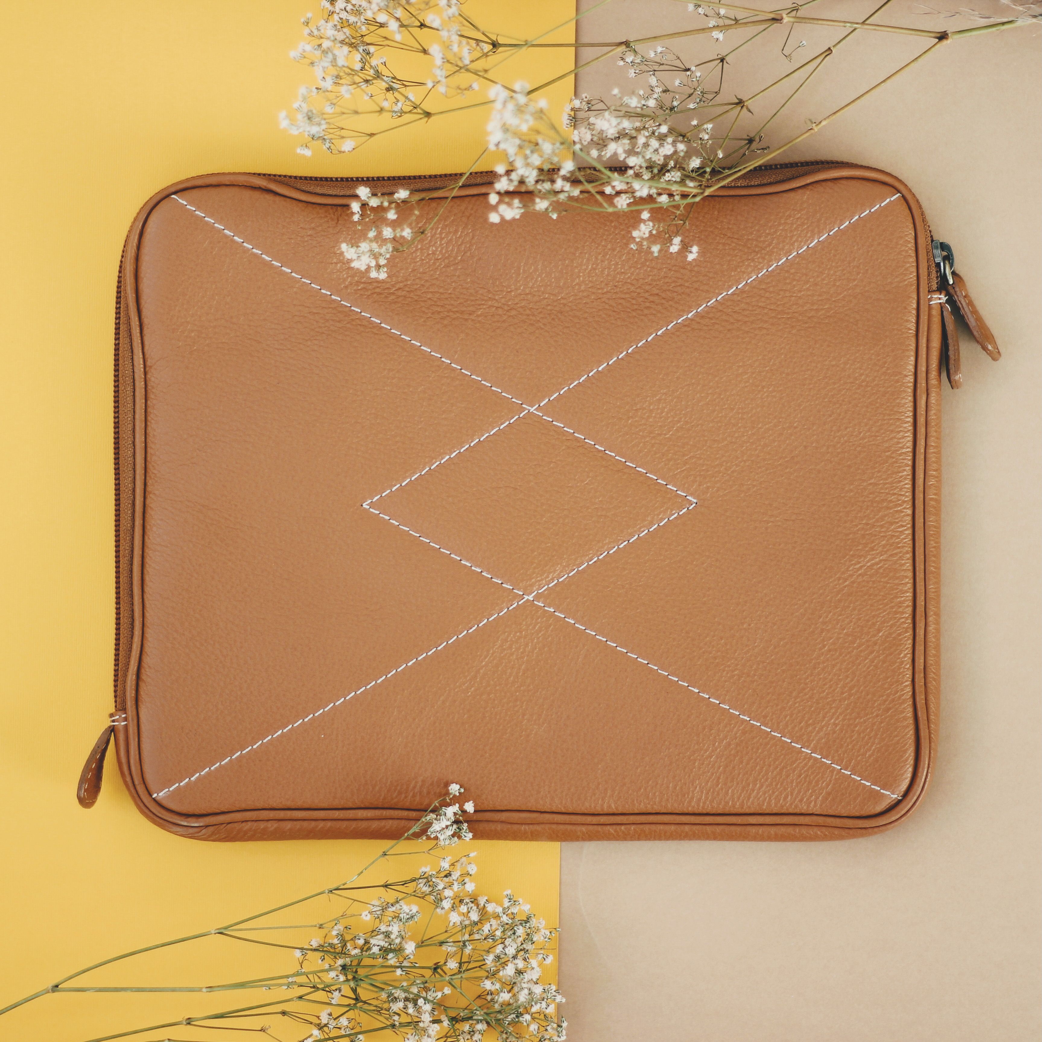 Top view of a stylish leather bag with stitching details on a pastel backdrop, decorated with white flowers.