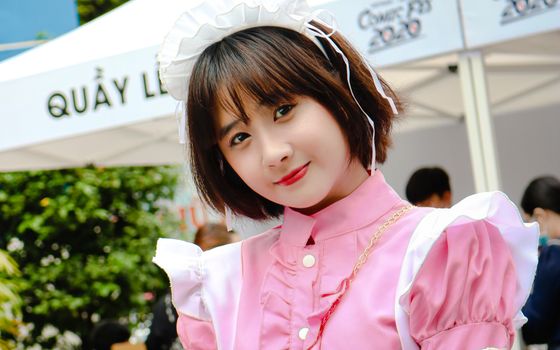 Cosplayer posing in a pink maid outfit at an outdoor cosplay festival, capturing a playful yet elegant look.