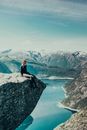 Woman in Black Jacket Sitting on Rock Formation Near Lake