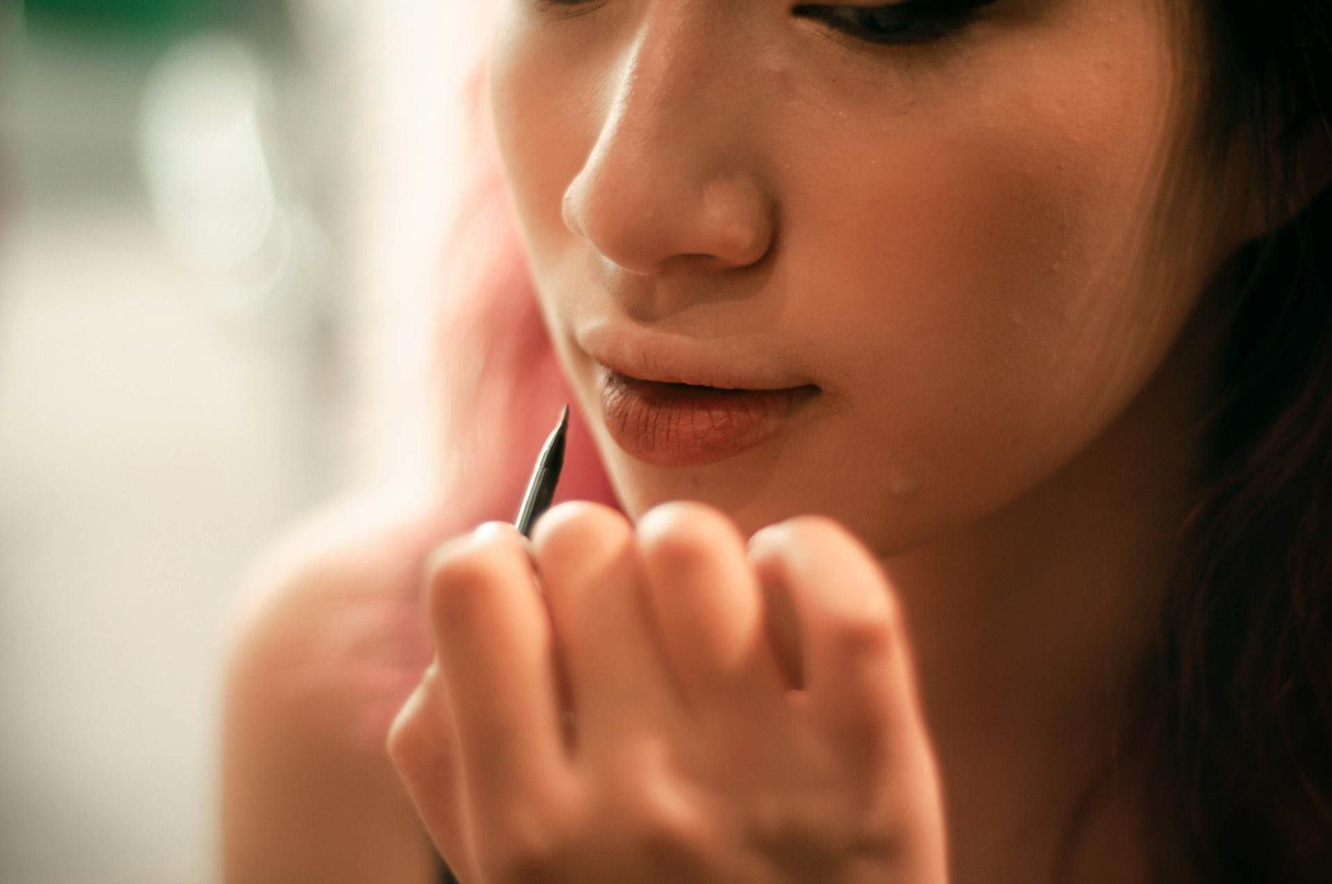 A woman applying lip liner on her lips with a pencil, captured in soft lighting indoors.