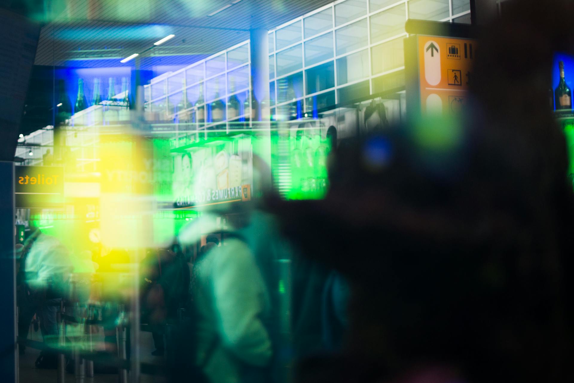 Blurred motion inside a bustling airport terminal with vibrant lights and signs.