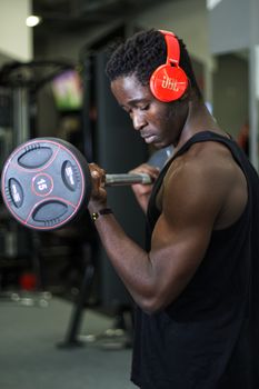 African American man weightlifting at a gym with headphones, focused and determined.
