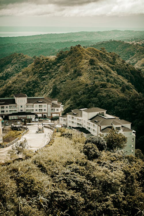 Scenic view of aged house exteriors between road and mounts with lush green trees in daylight