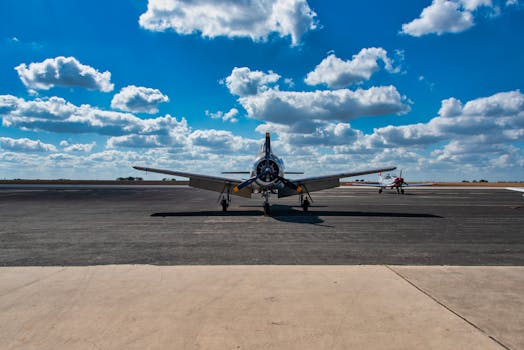 A vintage airplane parked on a runway under a vibrant blue sky with scattered clouds.