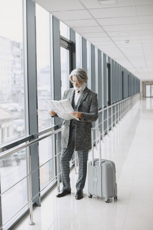 Free Businessman in a gray suit reading a newspaper in an airport corridor with suitcase. Stock Photo