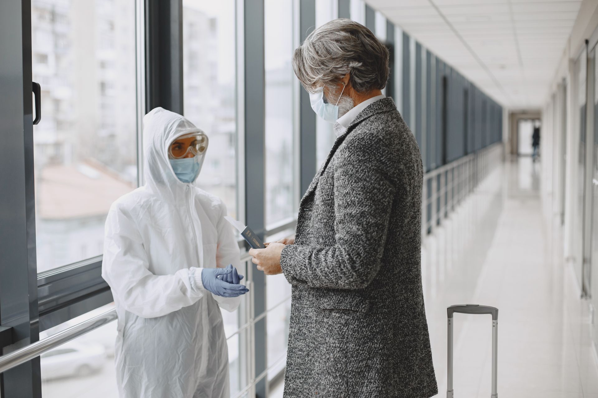 Two masked individuals in a hallway engaging over travel documents, representing travel during health crises.