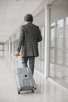 Elegant man in suit walking through airport corridor with suitcase, back view.