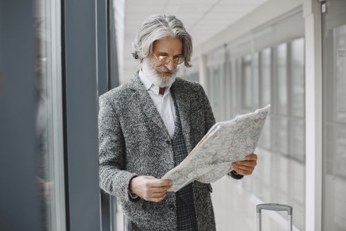 Free Elderly man with suitcase reads map in a bright airport corridor, planning his journey. Stock Photo