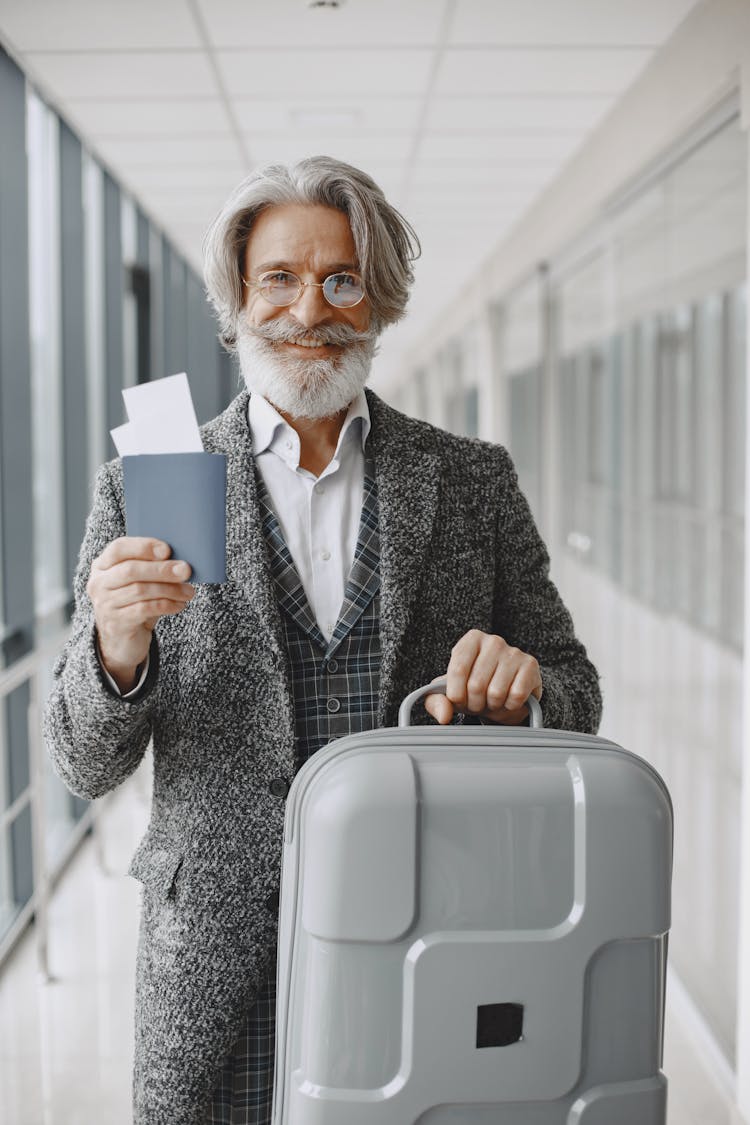 An Elderly Man With Eyeglasses Holding His Luggage And Passport