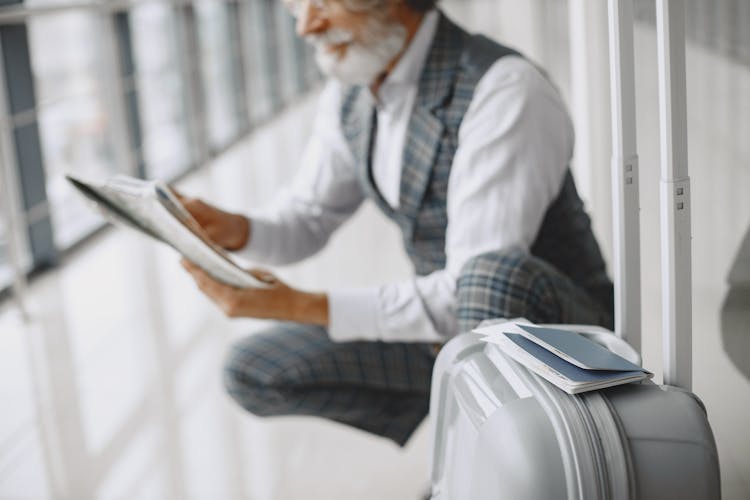 A Man Holding A Paper Sitting Near His Luggage