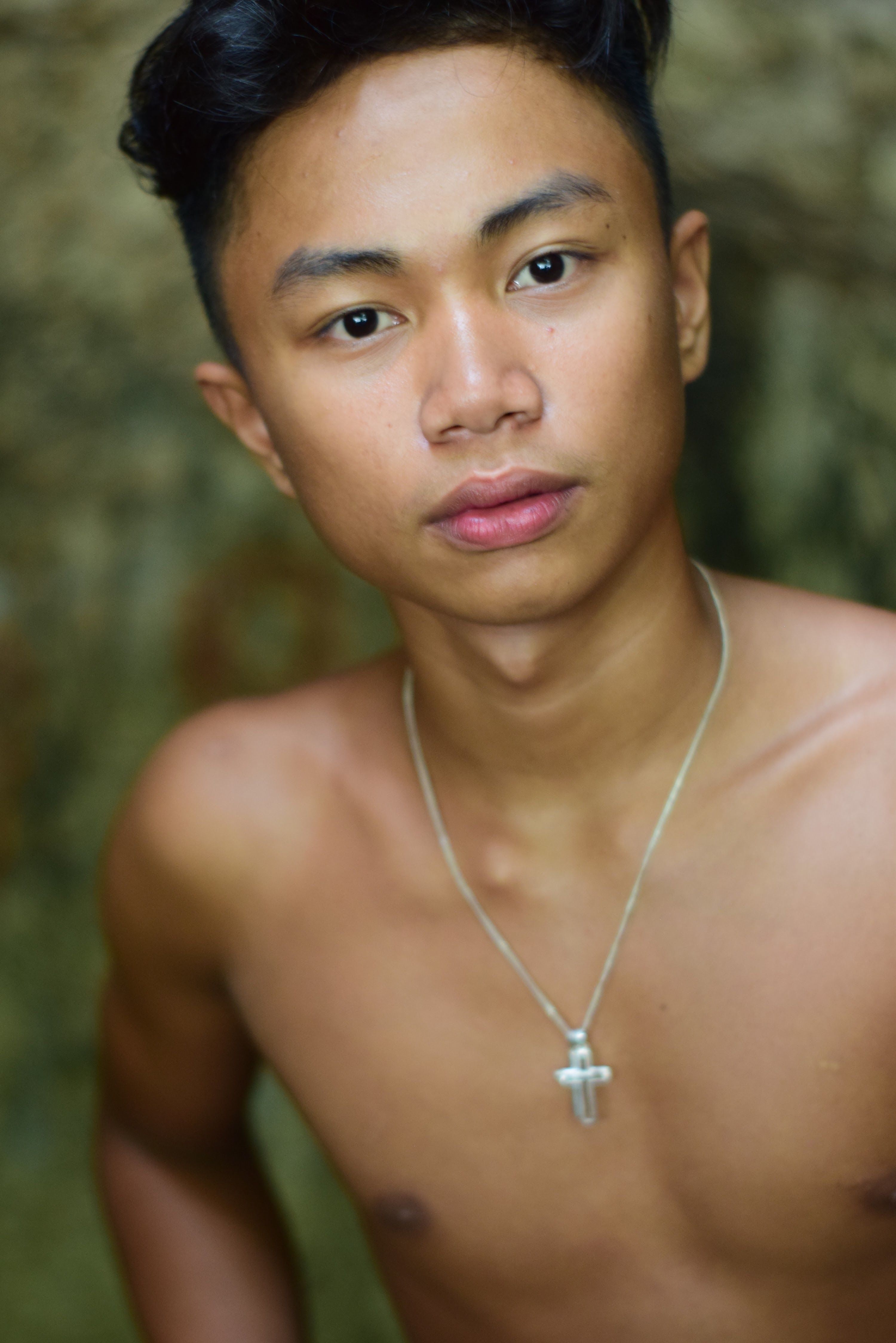 Portrait of a young man posing outdoors with a silver necklace.