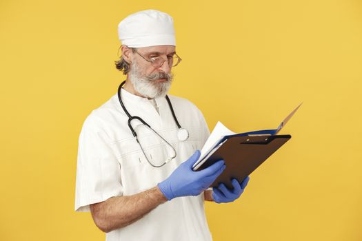 A bearded male doctor with stethoscope reviews medical documents on a yellow background.