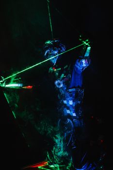 A striking image of a futuristic performer in a neon costume playing a musical instrument with lasers in a dark setting. — photo by Jeniya Orlova