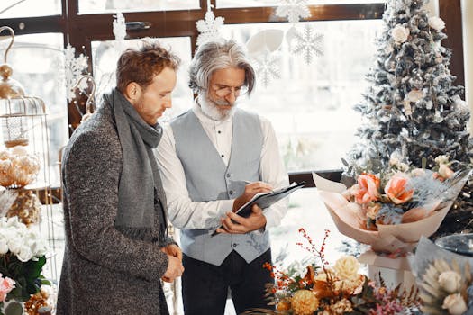 Two men discussing flower arrangements near a Christmas tree indoors.