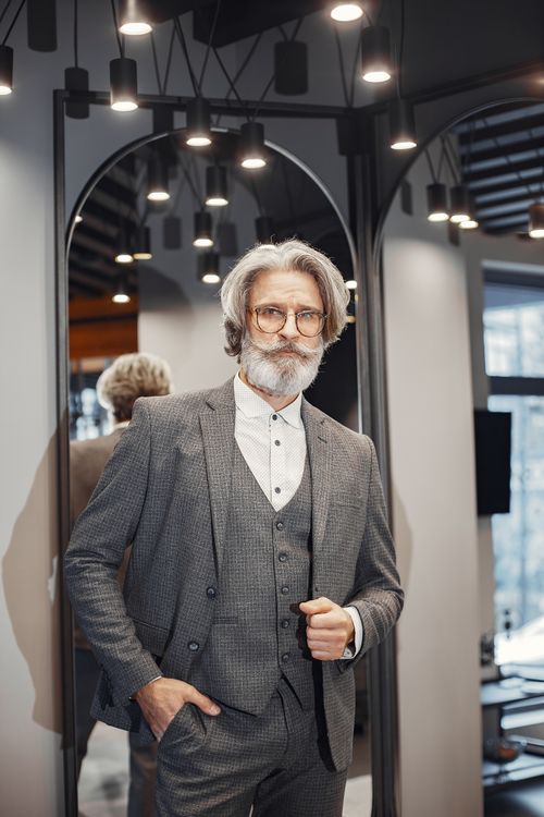 Free Elegant senior gentleman with glasses and beard in a tailored suit, posing confidently indoors. Stock Photo