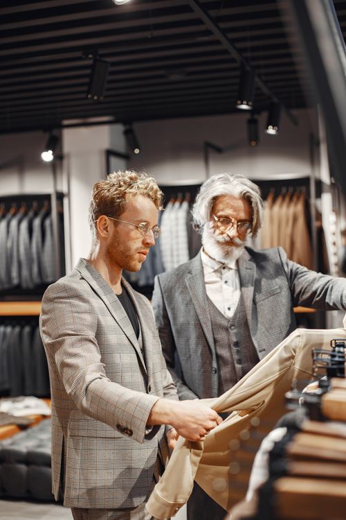 Free Two adult men examining suits in a stylish store with racks of clothing in the background. Stock Photo