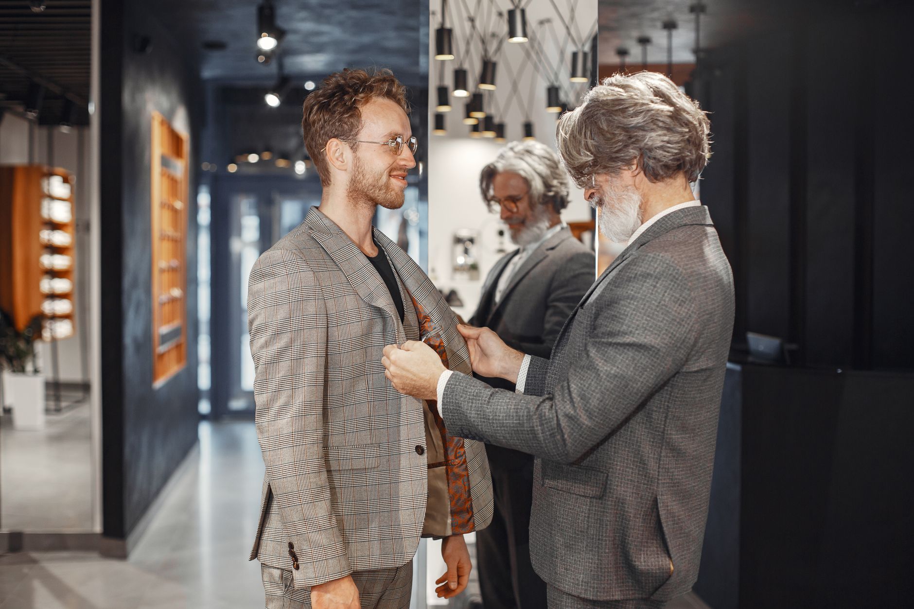 A tailor adjusts a customer's suit jacket in a stylish, modern boutique store setting.
