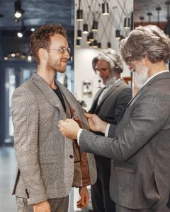 A tailor adjusts a customer's suit jacket in a stylish, modern boutique store setting.