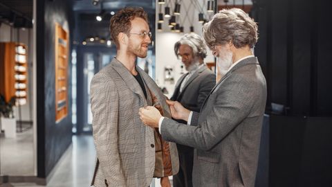 A tailor adjusts a customer's suit jacket in a stylish, modern boutique store setting.