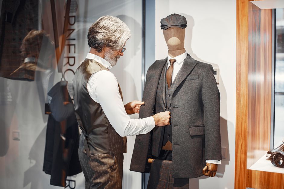 Man adjusting a tailored suit on a mannequin in a formal wear store, highlighting fashion elegance and craftsmanship.