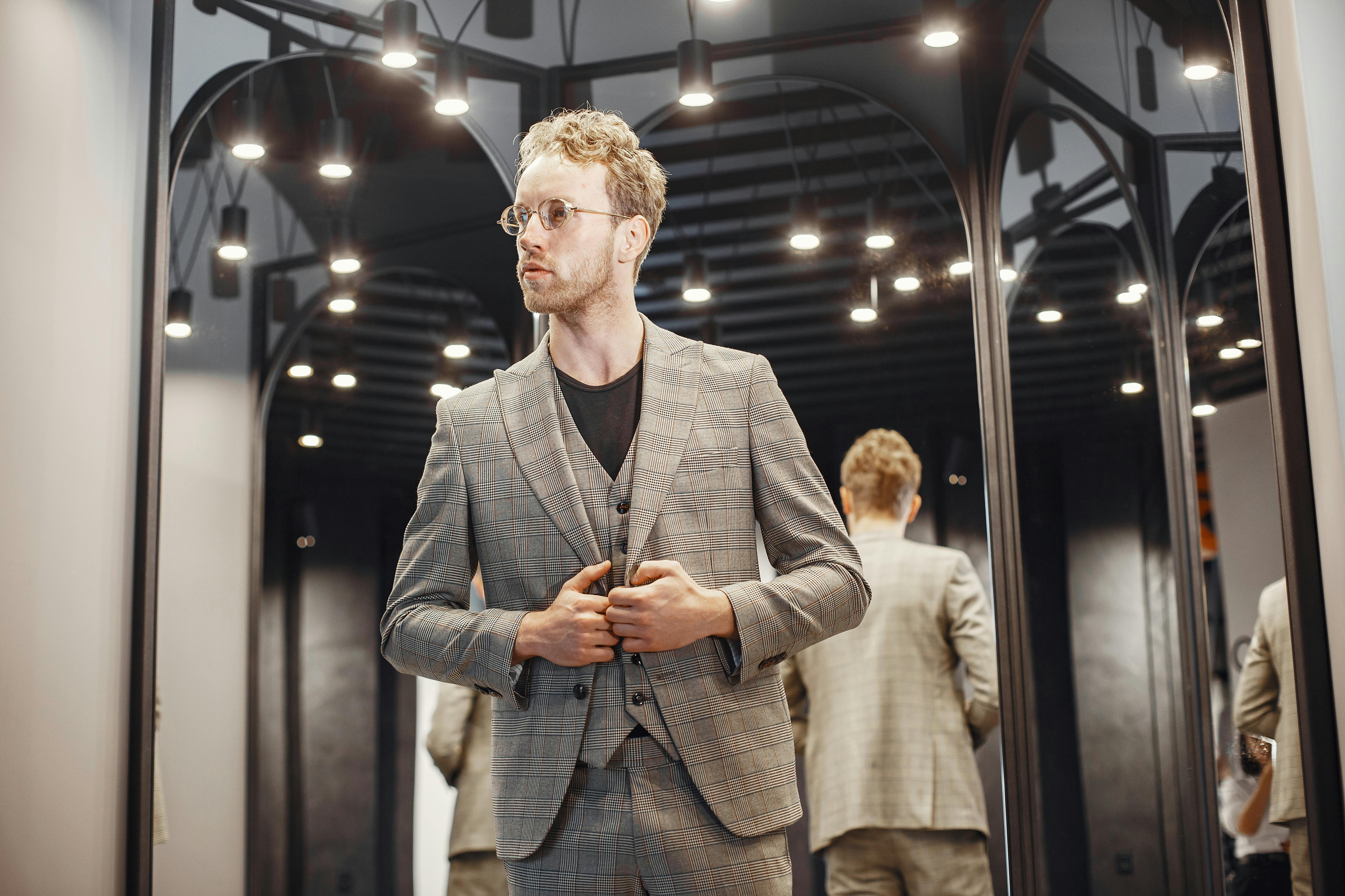 Elegant young man adjusts his suit in a well-lit dressing room. Fashion and style concept.