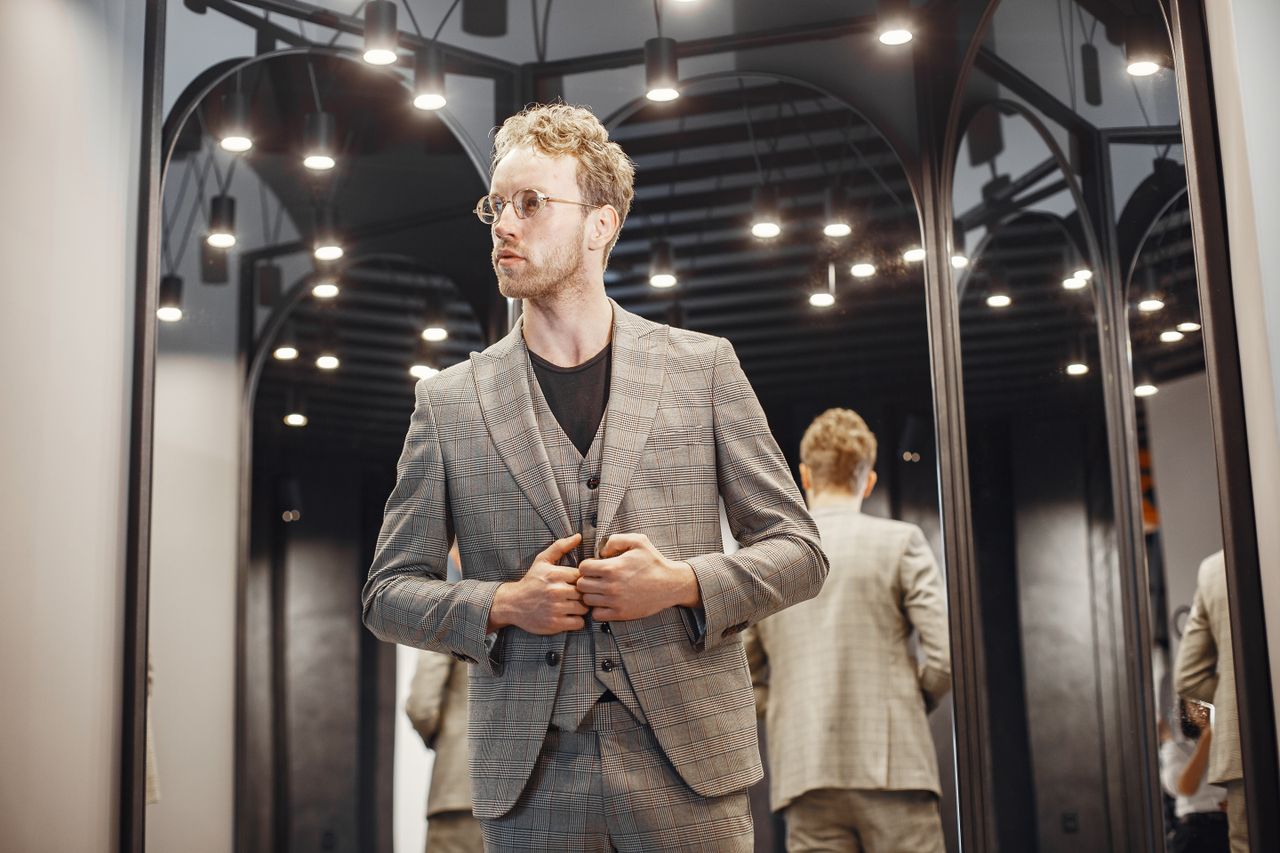 elegant young man adjusts his suit in a well lit dressing room fashion