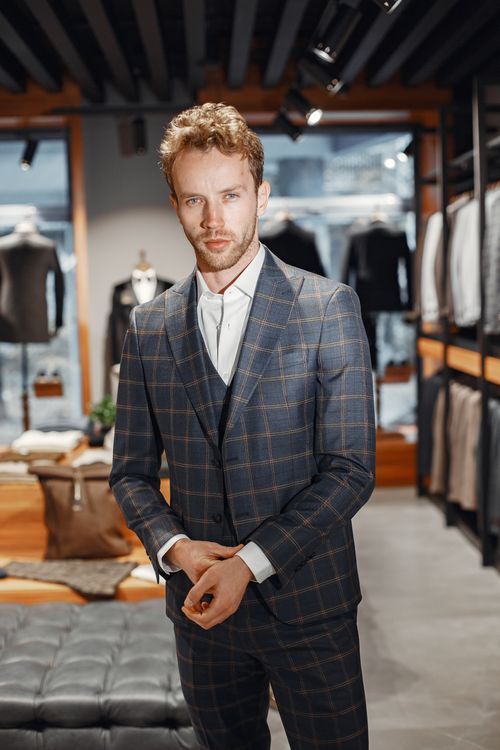 Free Handsome man in a checkered suit poses confidently in a modern store interior. Stock Photo