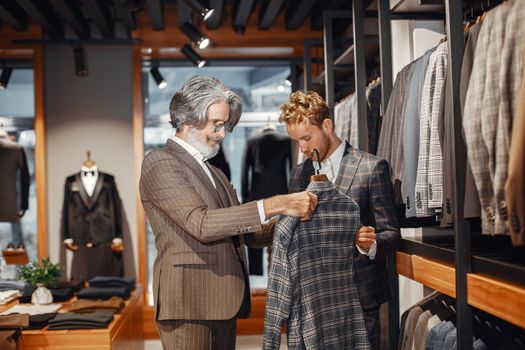 Two men choosing a suit in a stylish clothing boutique. Indoor shopping scene.