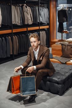 Man in a brown suit holding shopping bags in a luxury menswear store, showcasing elegance and fashion.