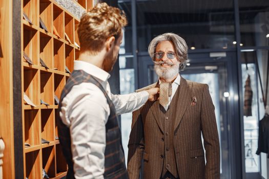 Elderly gentleman trying on a suit with assistance in a classy store. Elegant, formal atmosphere.