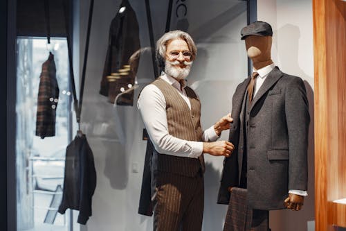 Elderly Man in Brown Vest Standing Beside a Mannequin in Gray Suit 