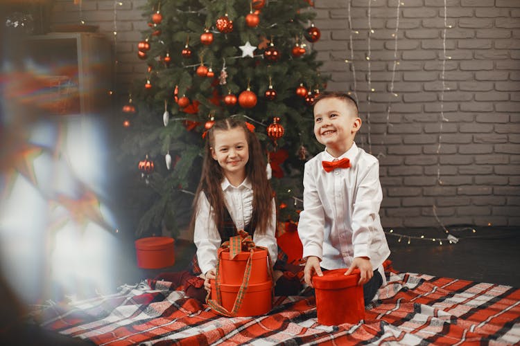 Happy Kids Sitting On Picnic Blanket While Holding Their Christmas Presents