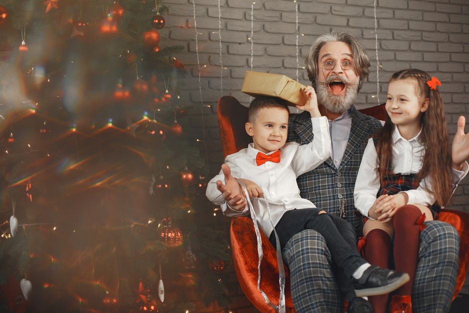 Happy family with grandfather and kids celebrating Christmas by the decorated tree.