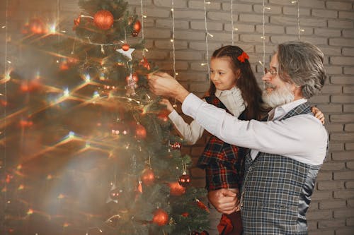 Grandfather and Granddaughter Decorating Christmas Tree with Red Baubles