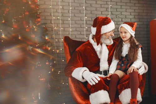 Free A child sitting on Santa Claus's lap, surrounded by holiday decorations. Stock Photo
