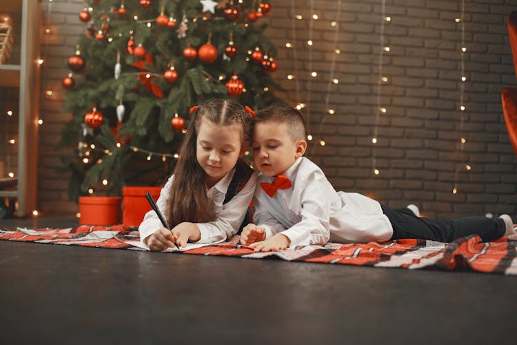 Children Drawing On Blanket Next To Christmas Tree