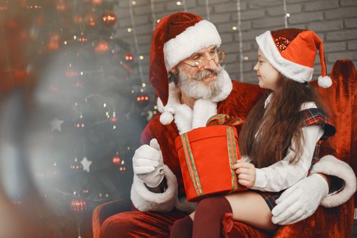 Free A cheerful girl receives a gift from Santa Claus beside a decorated Christmas tree. Stock Photo