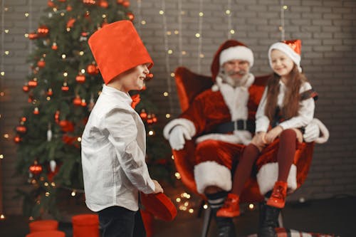 Boy in a Red Hat and Santa Clause with a Girl Sitting on his Lap 