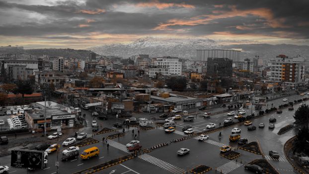 Aerial view of Kabul city skyline with traffic at sunset, featuring mountains and urban architecture.
