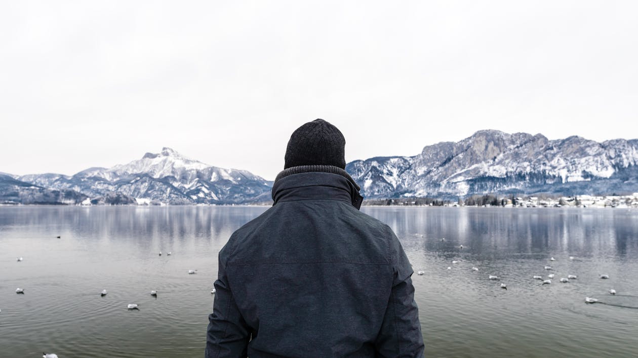 Free Back View of a Person in Winter Clothes Standing near the Lake Stock Photo